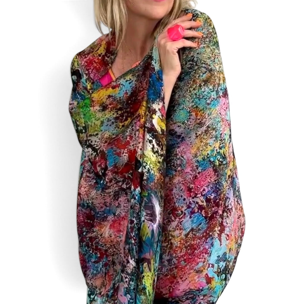 A woman wearing a vibrant, multicolored abstract print poncho or shawl against a plain white background.