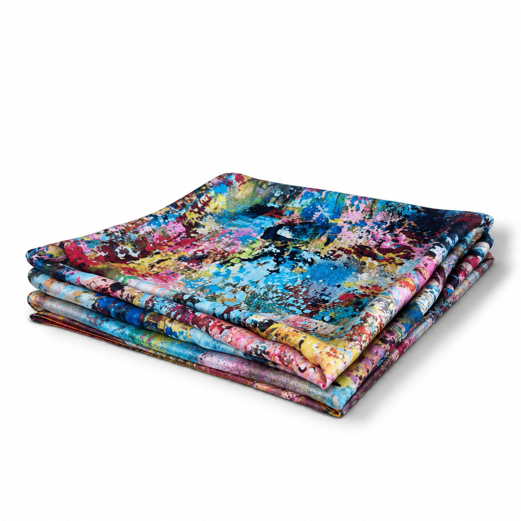 A stack of folded fabric napkins or table linens featuring a vibrant, multicolored abstract paint-splatter pattern, photographed on a clean white background.