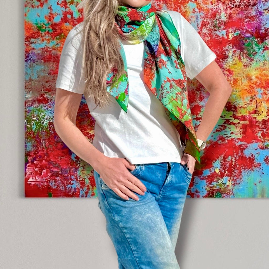 Model wearing a colorful Natalia Brooks silk scarf in front of the original abstract painting