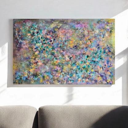 A large rectangular abstract canvas painting with a dense, textured floral-like pattern in pastel blue, purple, green, yellow, and pink tones, displayed on a white wall above a gray sofa.
