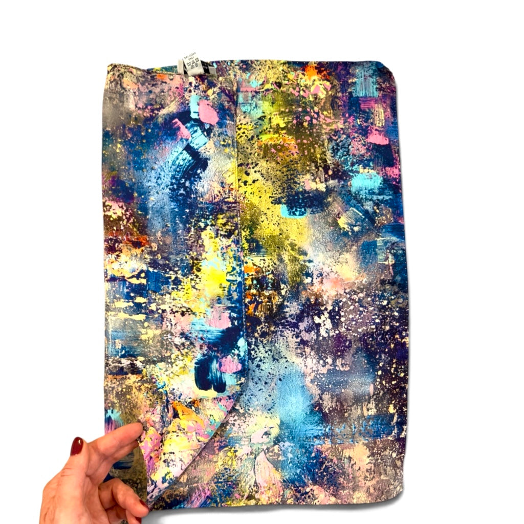 A fabric pouch with a colorful abstract paint splatter pattern, held open by a hand with red painted fingernails against a plain white background.