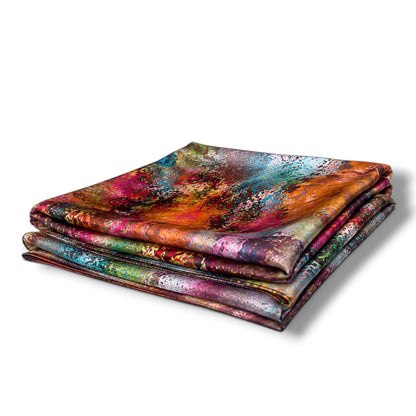 A stack of four folded square scarves with an abstract, multicolored paint-splatter pattern, displayed on a clean white background.