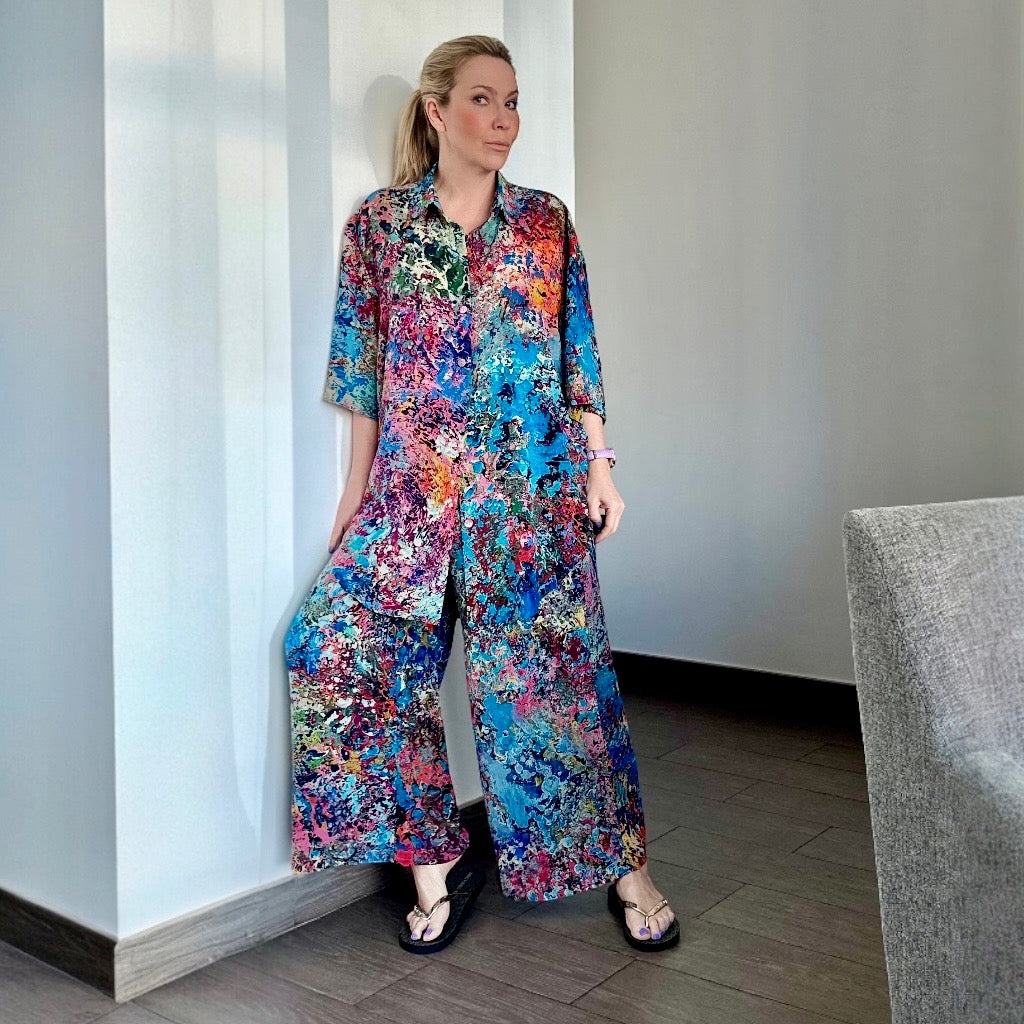 Woman wearing a colorful silk floral dress standing against a white wall.