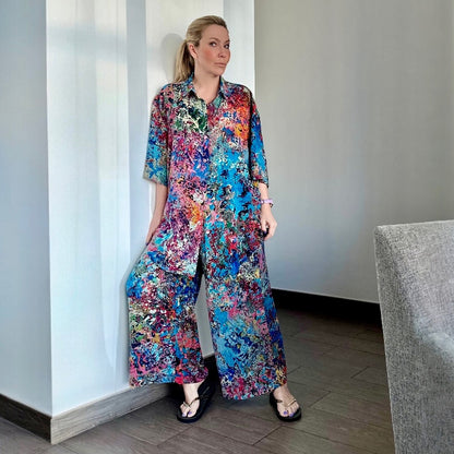 Woman wearing a colorful silk floral dress standing against a white wall.