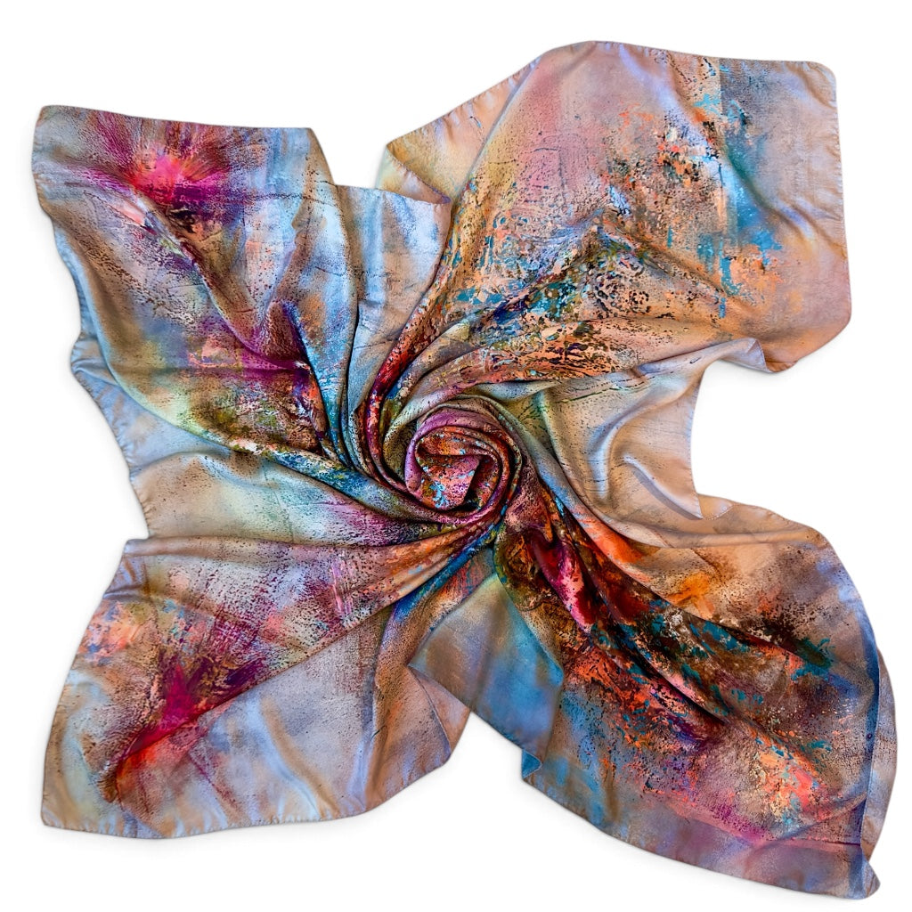 A square silk scarf with an abstract, painterly print featuring a spiral swirl of blue, pink, purple, orange, and gold tones, arranged in a neat cross-like shape on a white background.