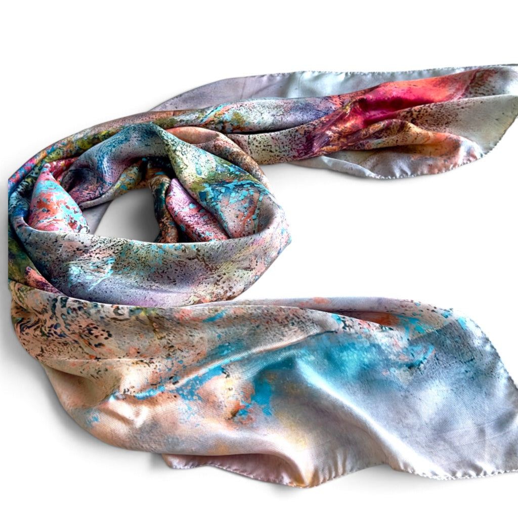 A lightweight silk scarf with an abstract, painterly pattern in shades of blue, pink, purple, and gold, draped elegantly on a plain white background.