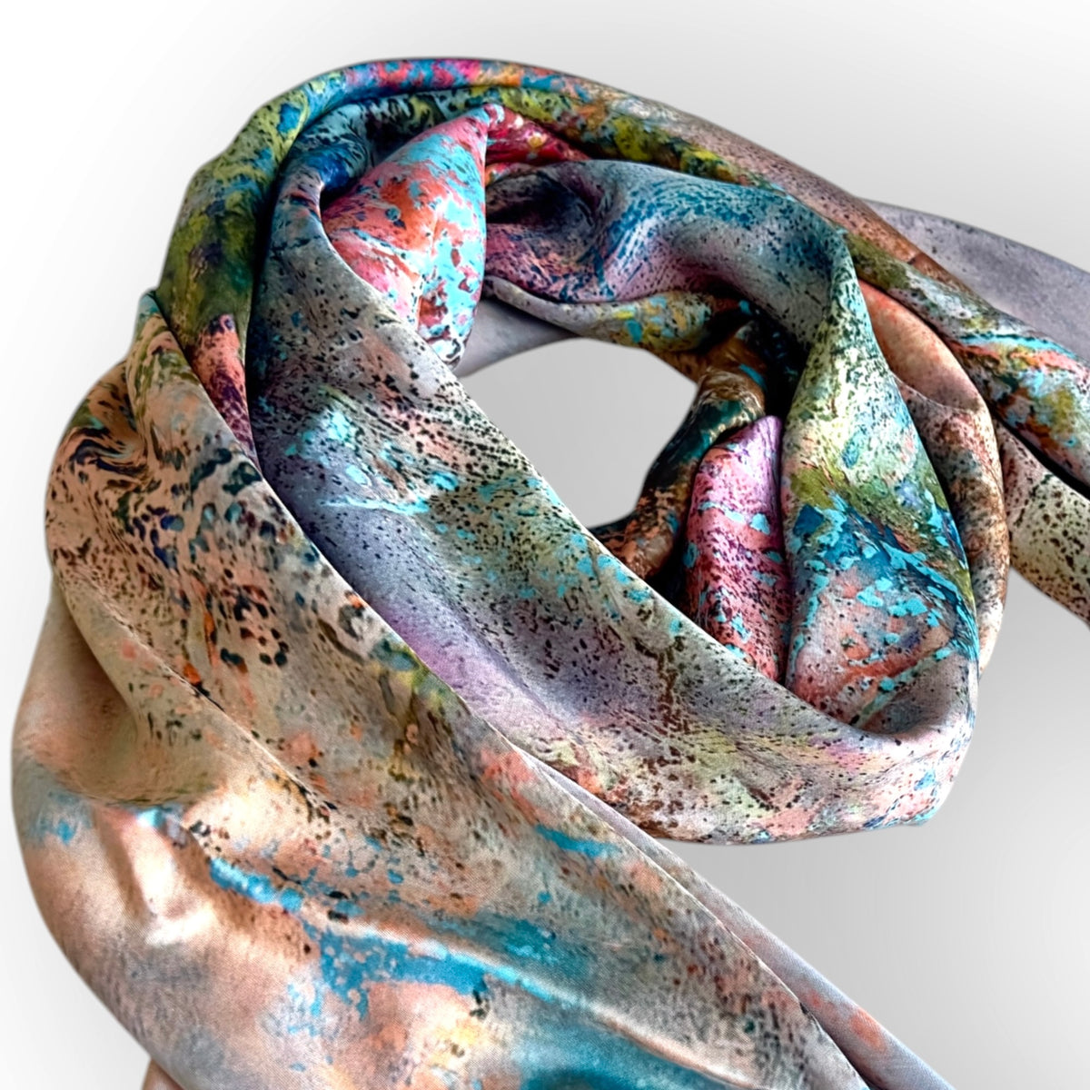 A lightweight silk scarf with a multicolor abstract print, featuring shades of teal, pink, gold, and purple, styled in a loose knot against a light gray background.