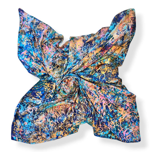A square scarf with a vibrant, multicolored abstract paint-splatter pattern, styled in a twisted knot on a clean white background.