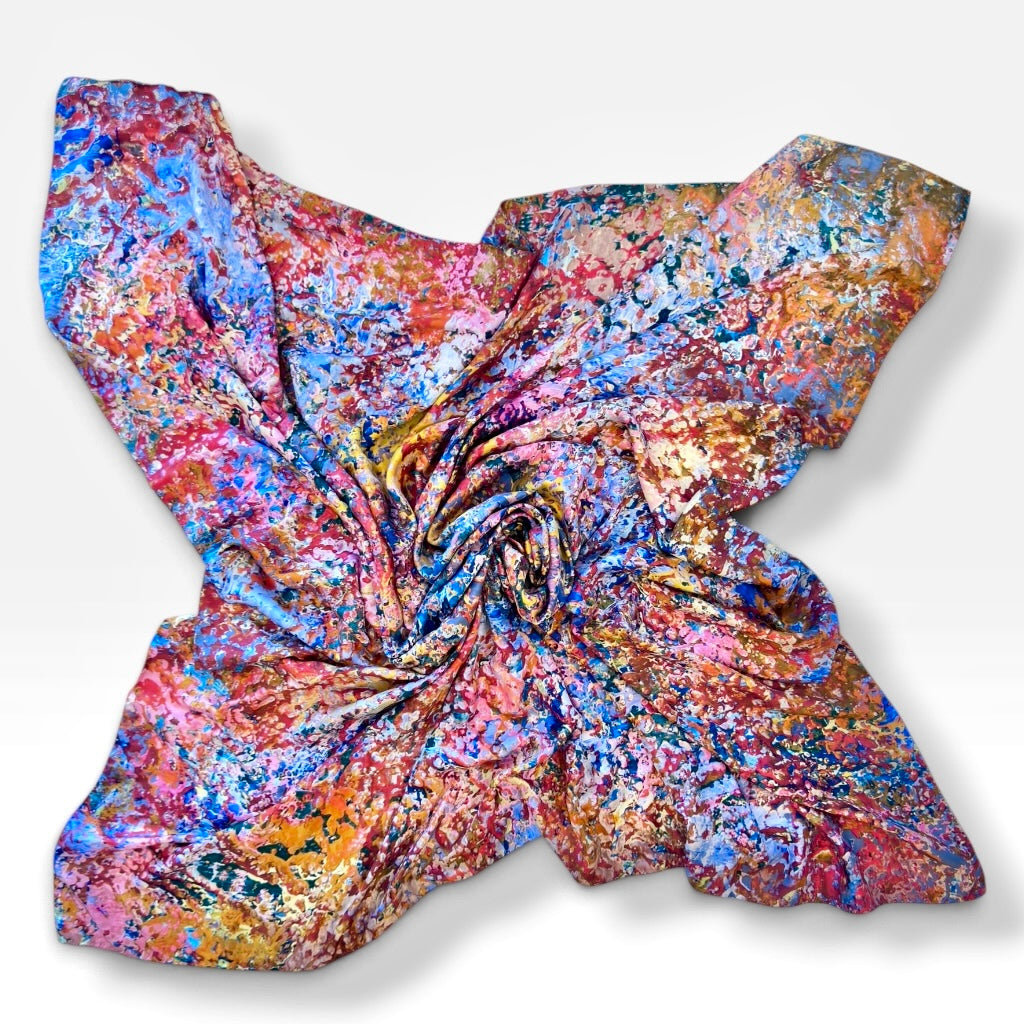 A square scarf with a vibrant, multicolored abstract paint-splatter pattern, arranged in a spiral on a light gray background.
