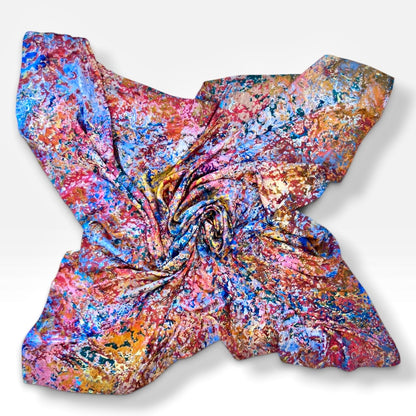 A square scarf with a vibrant, multicolored abstract paint-splatter pattern, arranged in a spiral on a light gray background.
